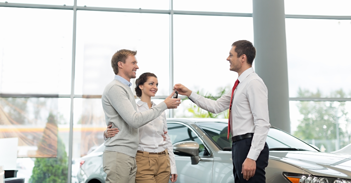 car salesman handing keys to a couple